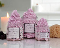 Three jars of pink whipped soap with decorative labels on a reflective surface.