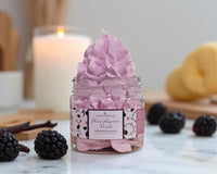 Jar of pink whipped soap with blackberries and vanilla beans on a marble surface.