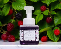 Foaming hand soap bottle with black raspberry and vanilla label in front of blackberries and green leaves.