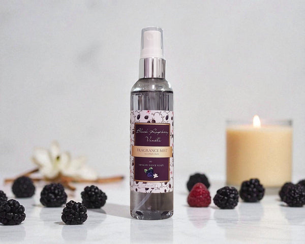 Bottle of black raspberry vanilla fragrance mist with berries and a candle on a light surface.