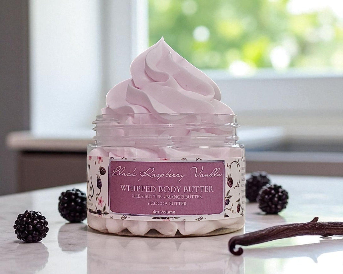 Jar of Black Raspberry Vanilla whipped body butter with black raspberries and vanilla beans on a marble surface.