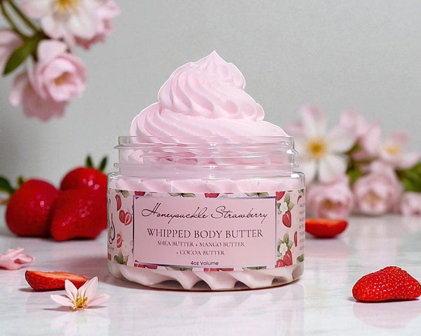 Jar of strawberry and honeysuckle scented whipped body butter with strawberries and flowers in the background
