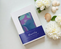 Coconut milk soap bar with packaging on a white surface surrounded by flowers and shells