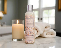 Body wash bottle with floral design on a marble surface next to a candle and towel