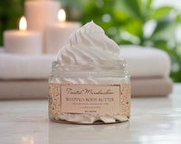 Jar of whipped body butter with a label on a surface with candles in the background