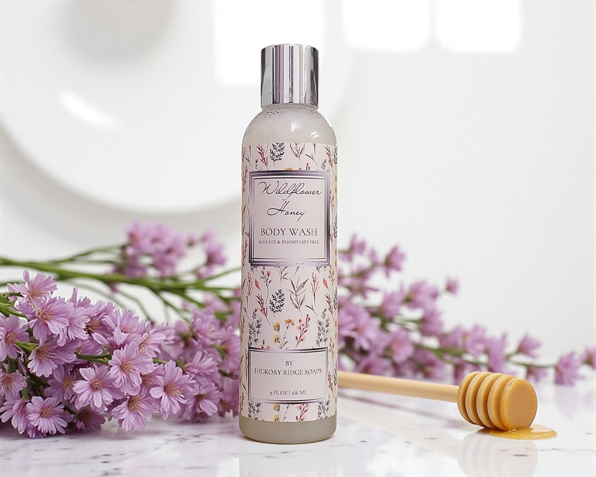 Body wash bottle with floral design on label, surrounded by pink flowers and a wooden spoon.